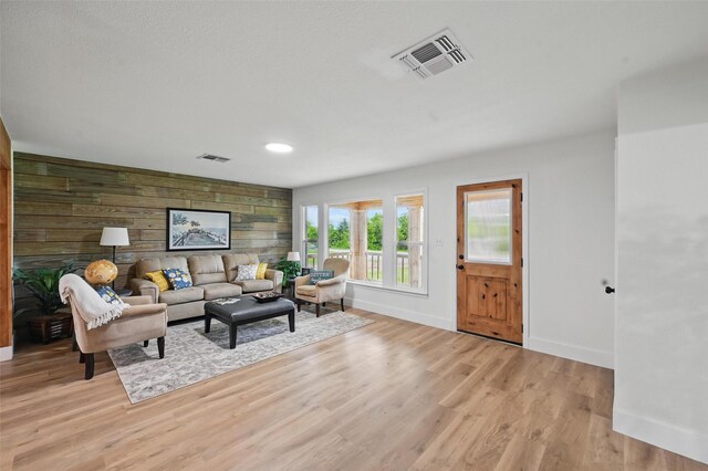 living area featuring baseboards, visible vents, wood walls, and light wood-style floors