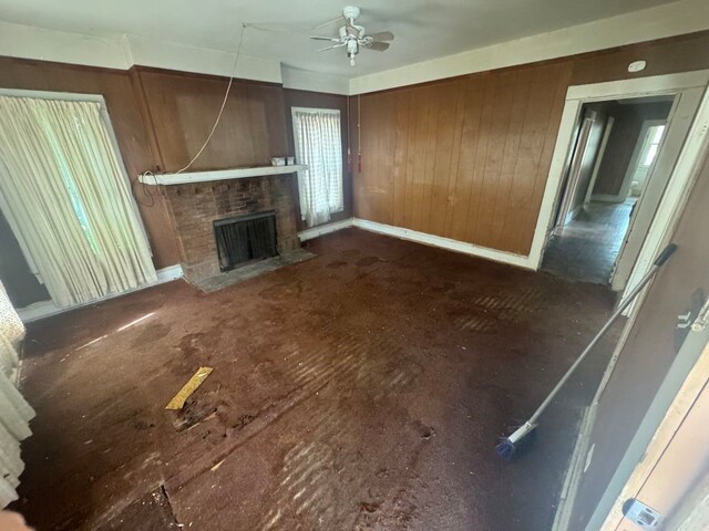 unfurnished living room featuring baseboards, ceiling fan, wooden walls, and a fireplace