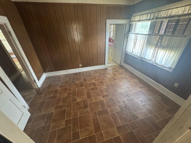 empty room featuring wooden walls, baseboards, and brick patterned floor