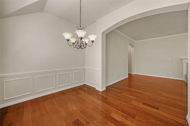 unfurnished dining area featuring an inviting chandelier, arched walkways, wood finished floors, vaulted ceiling, and ornamental molding
