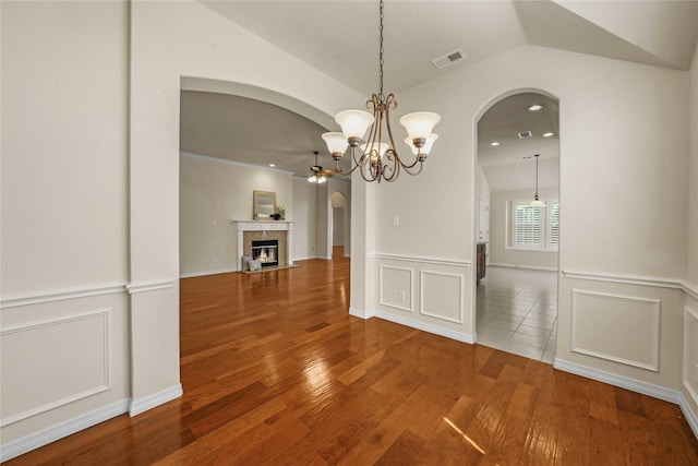 unfurnished dining area with visible vents, a fireplace with flush hearth, arched walkways, wood finished floors, and ceiling fan with notable chandelier