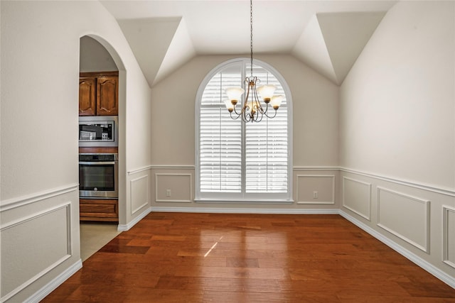 unfurnished dining area featuring a wainscoted wall, vaulted ceiling, wood finished floors, and a chandelier