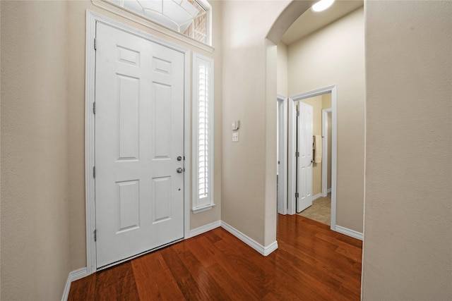 foyer with arched walkways, baseboards, and dark wood-style floors