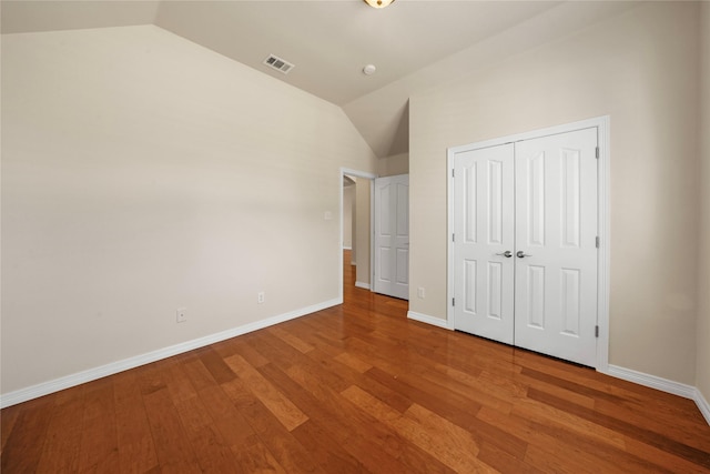 unfurnished bedroom with baseboards, visible vents, wood finished floors, and lofted ceiling