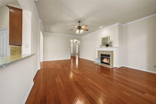 unfurnished living room with crown molding, arched walkways, ceiling fan, and wood finished floors
