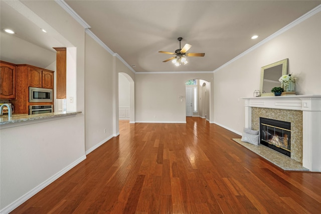 unfurnished living room featuring a ceiling fan, wood finished floors, baseboards, a tiled fireplace, and arched walkways