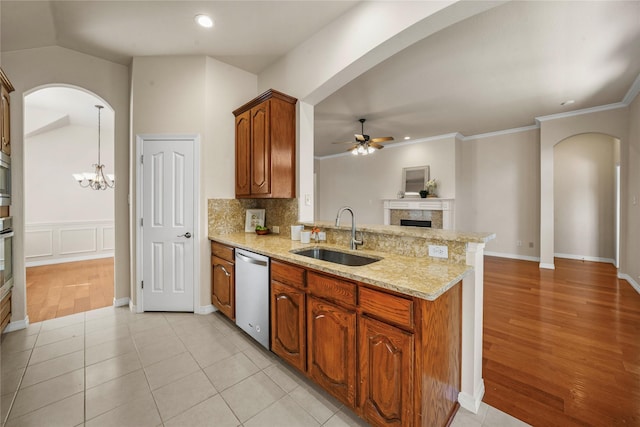 kitchen featuring a peninsula, ceiling fan with notable chandelier, a tiled fireplace, a sink, and appliances with stainless steel finishes