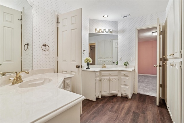 full bath with a sink, wood finished floors, two vanities, and wallpapered walls