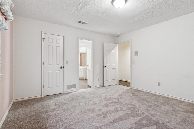 unfurnished bedroom with visible vents, connected bathroom, a textured ceiling, and carpet floors
