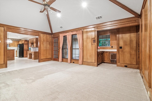 unfurnished living room featuring a ceiling fan, visible vents, high vaulted ceiling, wooden walls, and light carpet