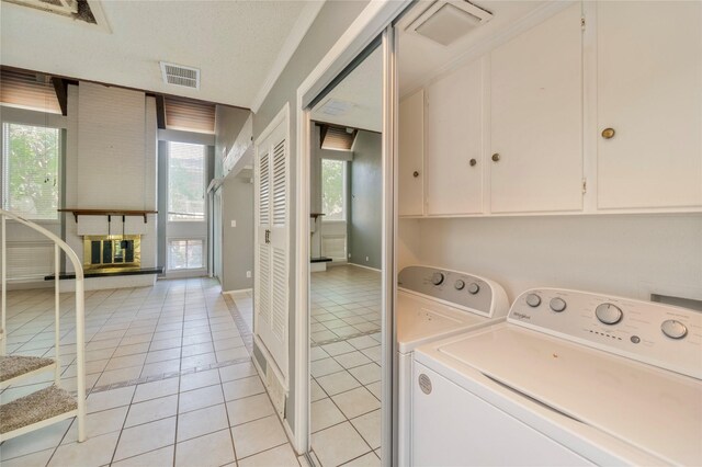 laundry area with visible vents, a fireplace, washing machine and clothes dryer, cabinet space, and light tile patterned floors