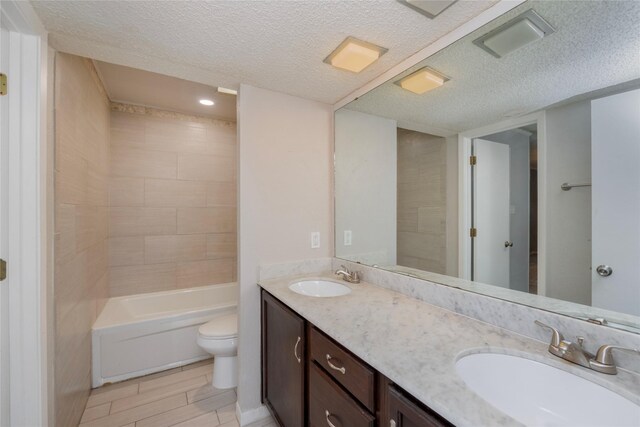 full bath with double vanity, a sink, a textured ceiling, and toilet