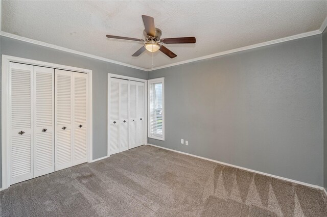 unfurnished bedroom with carpet floors, a textured ceiling, two closets, baseboards, and ornamental molding