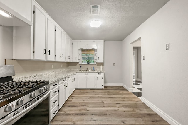 3544 Parker Rd E, Haltom City, TX 76117 - kitchen with a textured ceiling, white cabinets, stainless steel range with gas cooktop, under cabinet range hood, and light wood-style flooring