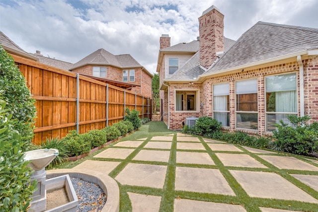 back of house featuring a patio, brick siding, a shingled roof, and a fenced backyard
