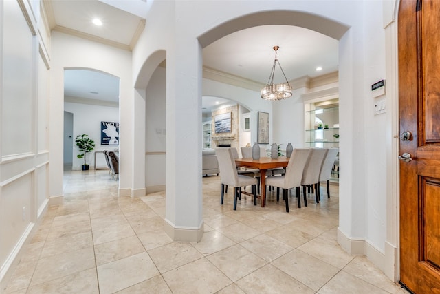 dining space featuring an inviting chandelier, arched walkways, baseboards, light tile patterned floors, and ornamental molding