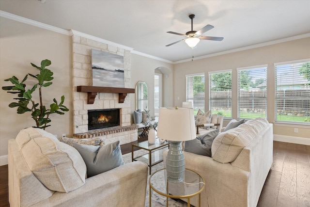 living room with crown molding, wood finished floors, a fireplace, baseboards, and a ceiling fan