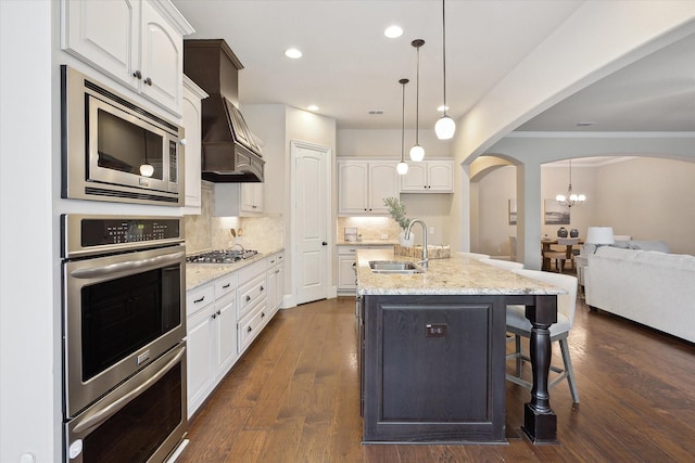 kitchen with white cabinets, a sink, arched walkways, stainless steel appliances, and custom range hood