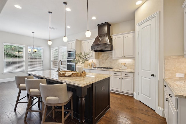 kitchen with decorative backsplash, a center island with sink, white cabinets, custom exhaust hood, and stainless steel appliances