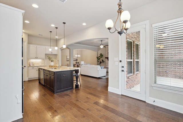 kitchen with stainless steel dishwasher, a sink, open floor plan, arched walkways, and ceiling fan with notable chandelier