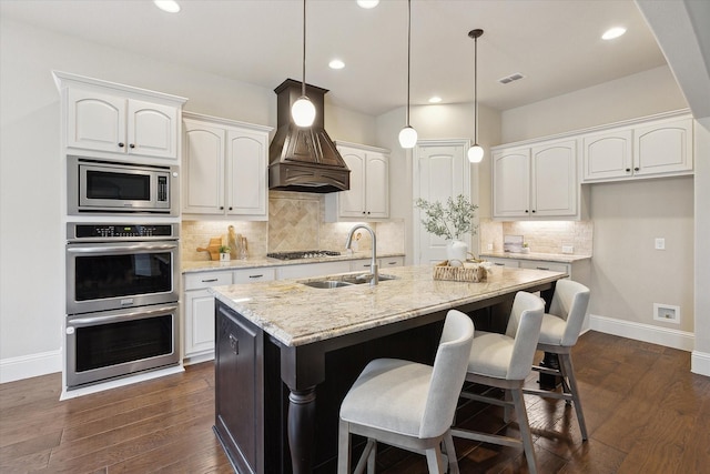 kitchen with visible vents, custom range hood, a sink, baseboards, and stainless steel appliances