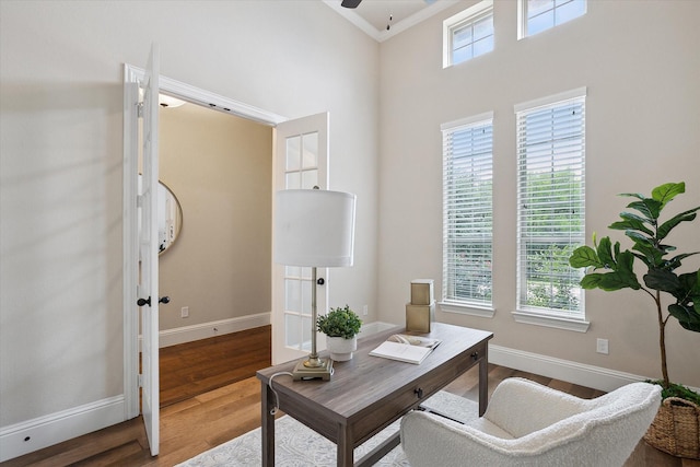 office space with a high ceiling, a ceiling fan, baseboards, wood finished floors, and ornamental molding