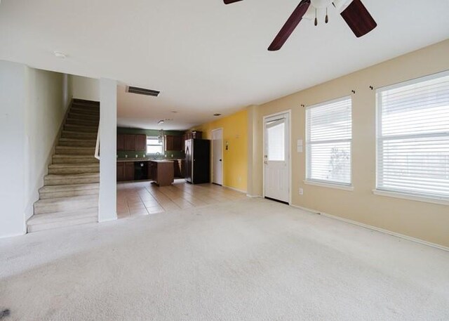 unfurnished living room with light colored carpet, stairs, a ceiling fan, baseboards, and visible vents