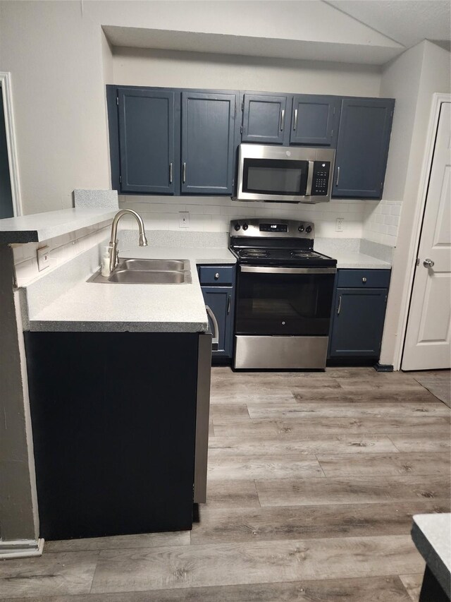 kitchen featuring a peninsula, light countertops, a sink, appliances with stainless steel finishes, and blue cabinetry