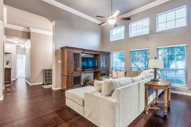 living room with crown molding, ceiling fan, dark wood-style floors, and a towering ceiling