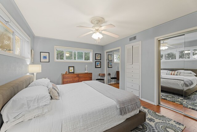 bedroom with visible vents, multiple closets, wood finished floors, baseboards, and a ceiling fan