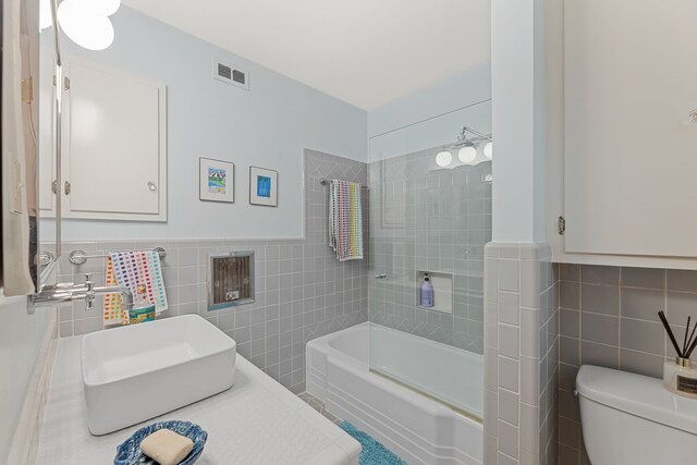 full bath featuring toilet, tile walls, a sink, and visible vents