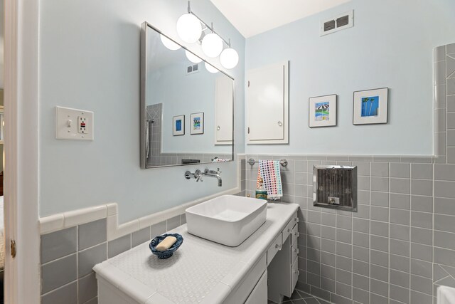 bathroom featuring visible vents, wainscoting, and tile walls
