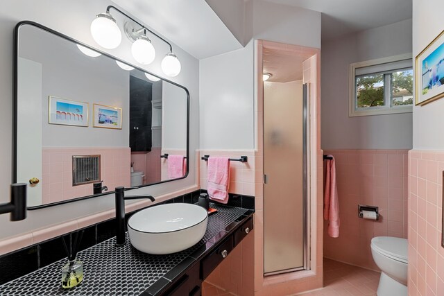 bathroom featuring tile walls, tile patterned flooring, wainscoting, a shower stall, and toilet