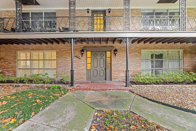 view of exterior entry featuring brick siding, a balcony, and covered porch