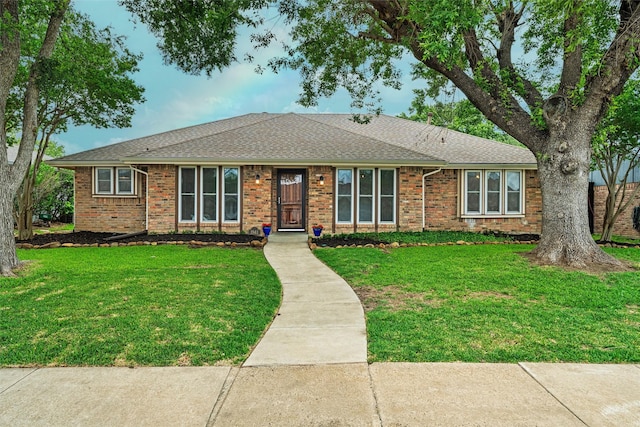 ranch-style home with brick siding, a shingled roof, and a front lawn