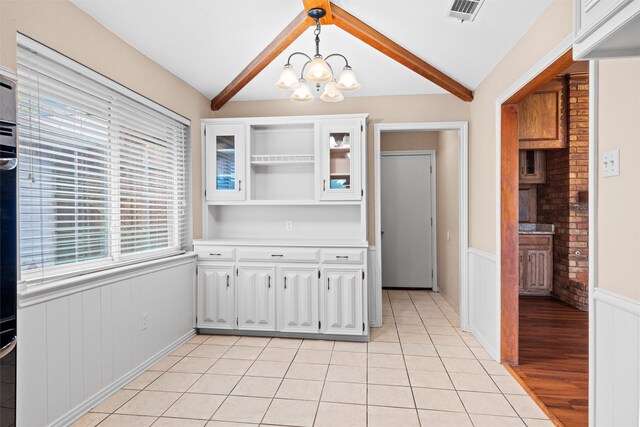 unfurnished dining area featuring visible vents, wainscoting, light tile patterned floors, lofted ceiling with beams, and a notable chandelier