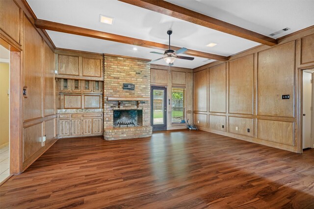 unfurnished living room featuring ceiling fan, beam ceiling, a brick fireplace, visible vents, and dark wood-style floors