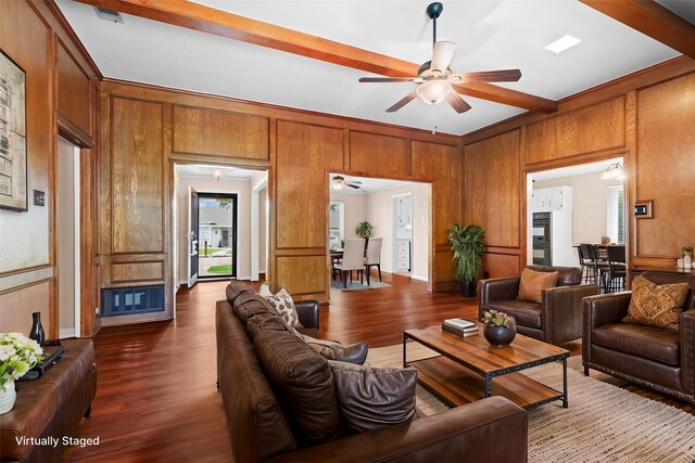 living room with a ceiling fan, dark wood-style flooring, beam ceiling, a fireplace with raised hearth, and wooden walls