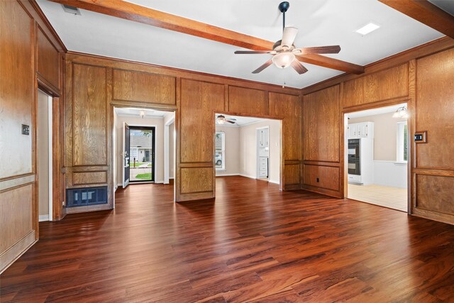 spare room with wood walls, beam ceiling, a fireplace, dark wood-style floors, and a ceiling fan