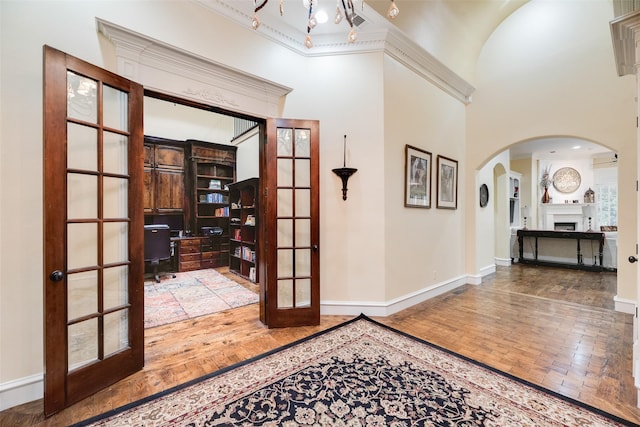 interior space featuring wood finished floors, baseboards, a high ceiling, french doors, and arched walkways