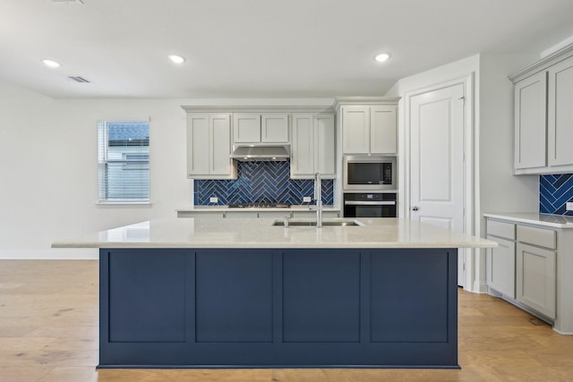 kitchen with under cabinet range hood, tasteful backsplash, a sink, light wood-style flooring, and stainless steel appliances