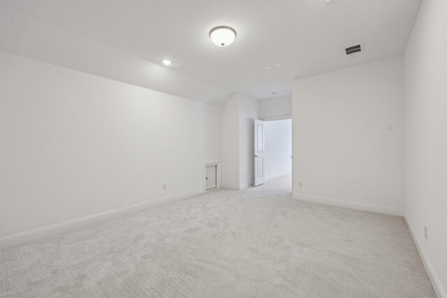 spare room featuring baseboards, vaulted ceiling, light colored carpet, and visible vents