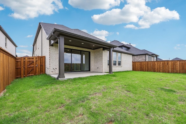 rear view of house featuring brick siding, a fenced backyard, a gate, a lawn, and a patio