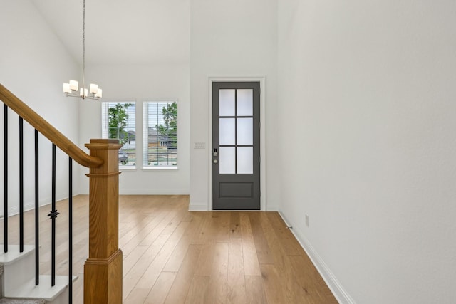 entryway featuring baseboards, light wood-type flooring, stairs, and a notable chandelier