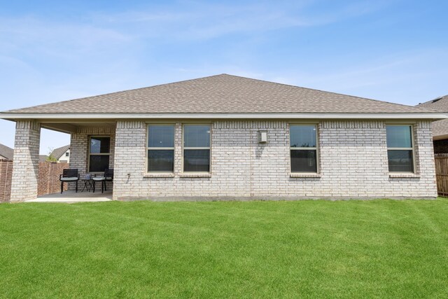 back of property featuring fence, roof with shingles, brick siding, a patio area, and a lawn