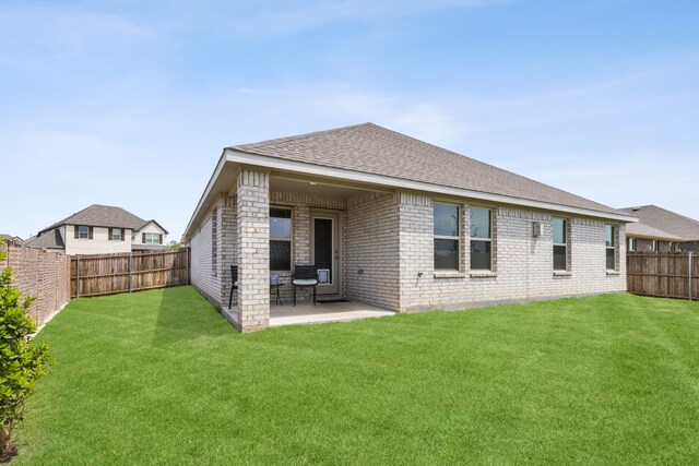 rear view of property with roof with shingles, brick siding, a fenced backyard, a patio area, and a yard