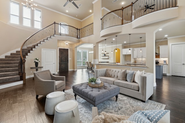 living area with arched walkways, a high ceiling, stairway, ceiling fan with notable chandelier, and ornamental molding