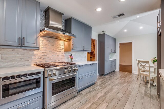kitchen with visible vents, high end stainless steel range, wall chimney range hood, light countertops, and light wood finished floors