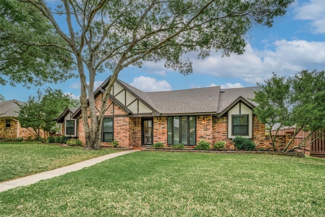 tudor house featuring roof with shingles, stucco siding, a front lawn, and brick siding