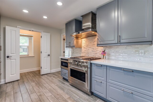 kitchen featuring wall chimney range hood, backsplash, baseboards, and high end stainless steel range oven